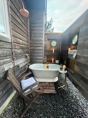 Une cabane en bois rustique avec une baignoire, un fauteuil suspendu et une petite table décorée de bougies.