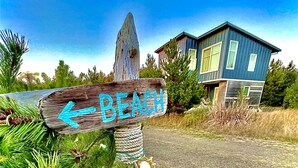 A wooden sign with "BEACH" written on it, pointing to the left, with a modern house in the background. - Ocean Views, Beach Path, Private + Pickleball + Nature Baths (Grayland)