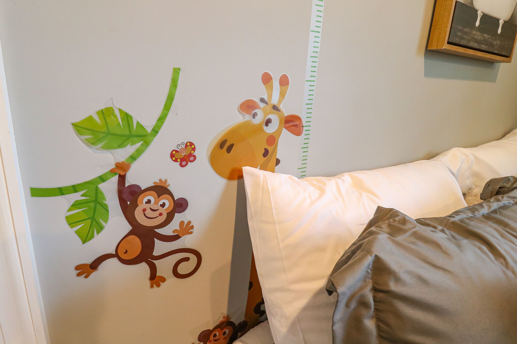 Uma parede infantil com adesivos de girafa, macaco e borboleta.