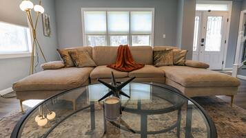 A modern living room with a sectional sofa, a glass coffee table with a metal sculpture, and a floor lamp.
