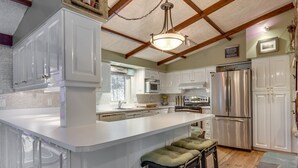 A spacious kitchen with white cabinetry, a large island, stainless steel appliances, and a wooden ceiling. - Lakefront tranquil chalet with spa near all outdoor activities (Val-Morin)