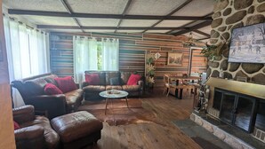A cozy living room with a stone fireplace, leather sofas, and a wooden dining table. - Lakefront tranquil chalet with spa near all outdoor activities (Val-Morin)