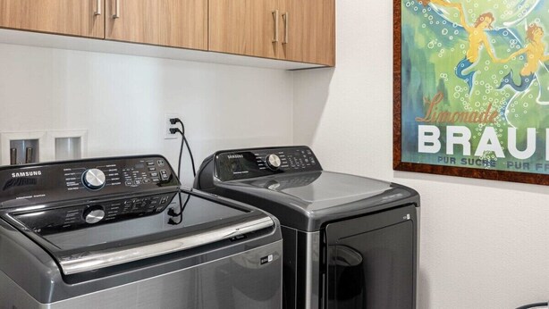 A laundry area with two Samsung washing machines and a Braun poster on the wall.