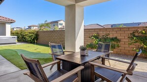 A patio with a wooden table and chairs, a small garden, and a brick wall.
