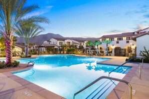 A swimming pool with a clear blue water surface, surrounded by lounge chairs and palm trees.