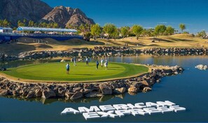 Un parcours de golf avec un étang, une montagne en arrière-plan et le texte « AMERICAN EXPRESS » inscrit sur l’eau.