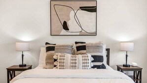 A neatly made bed with striped pillows, two bedside lamps, and a wall-mounted abstract artwork.