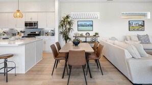 A modern kitchen with white cabinetry, a dining area with a table and chairs, and a living area with a sofa and cushions.