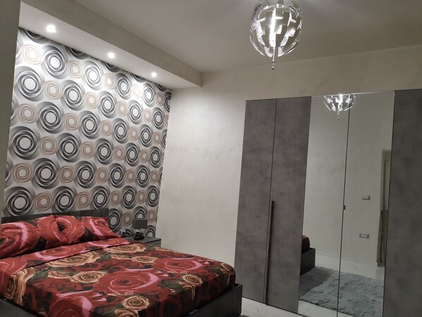 A bedroom with a bed, a wardrobe, a mirror, and a patterned wall.