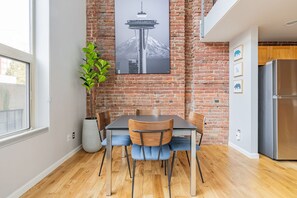 A modern kitchen with a brick wall, a stainless steel refrigerator, and a dining table with chairs. - Modern Loft in the Heart of Seattle (Seattle)