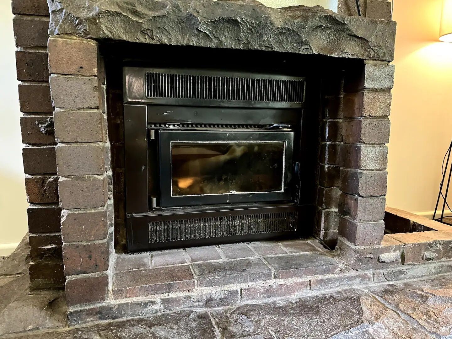 A stone fireplace with a black metal front, set in a brick wall.