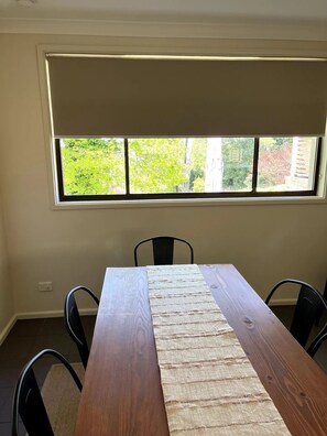 A dining room with a wooden table, four chairs, and a large window with a view of trees and a brick wall.