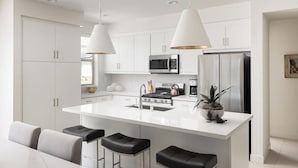 A modern kitchen with white cabinetry, stainless steel appliances, and a central island with bar stools. - Prime PGA West Escape, Pool, BBQ and Patio (La Quinta)