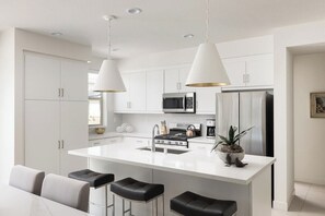 A modern kitchen with white cabinetry, stainless steel appliances, and a central island with bar stools. - Prime PGA West Escape, Pool, BBQ and Patio (La Quinta)