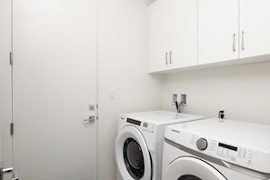A laundry room with two white washing machines, a white door, and white cabinets. - Prime PGA West Escape, Pool, BBQ and Patio (La Quinta)