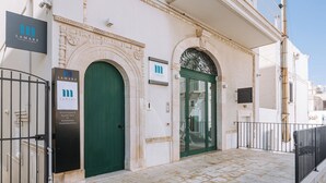 Fachada de edificio con dos puertas verdes, un acceso empedrado en piedra y una barandilla de metal.