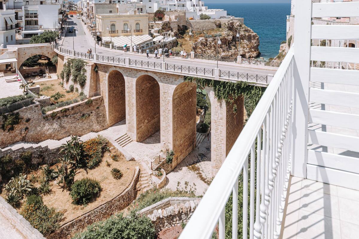 Un poble costaner amb edificis blancs, un pont i un cel blau clar.