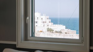 Una ventana con vistas a una zona costera, un edificio blanco y un cielo despejado.