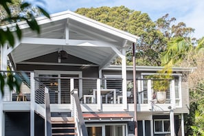 Enjoy a tranquil retreat in this two-story house with a shaded outdoor seating area and lush surroundings.