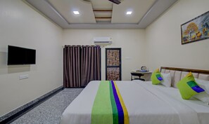 Habitación de hotel con cama, televisor de pantalla plana en la pared, una mesita con hervidor y una puerta con felpudo decorativo.