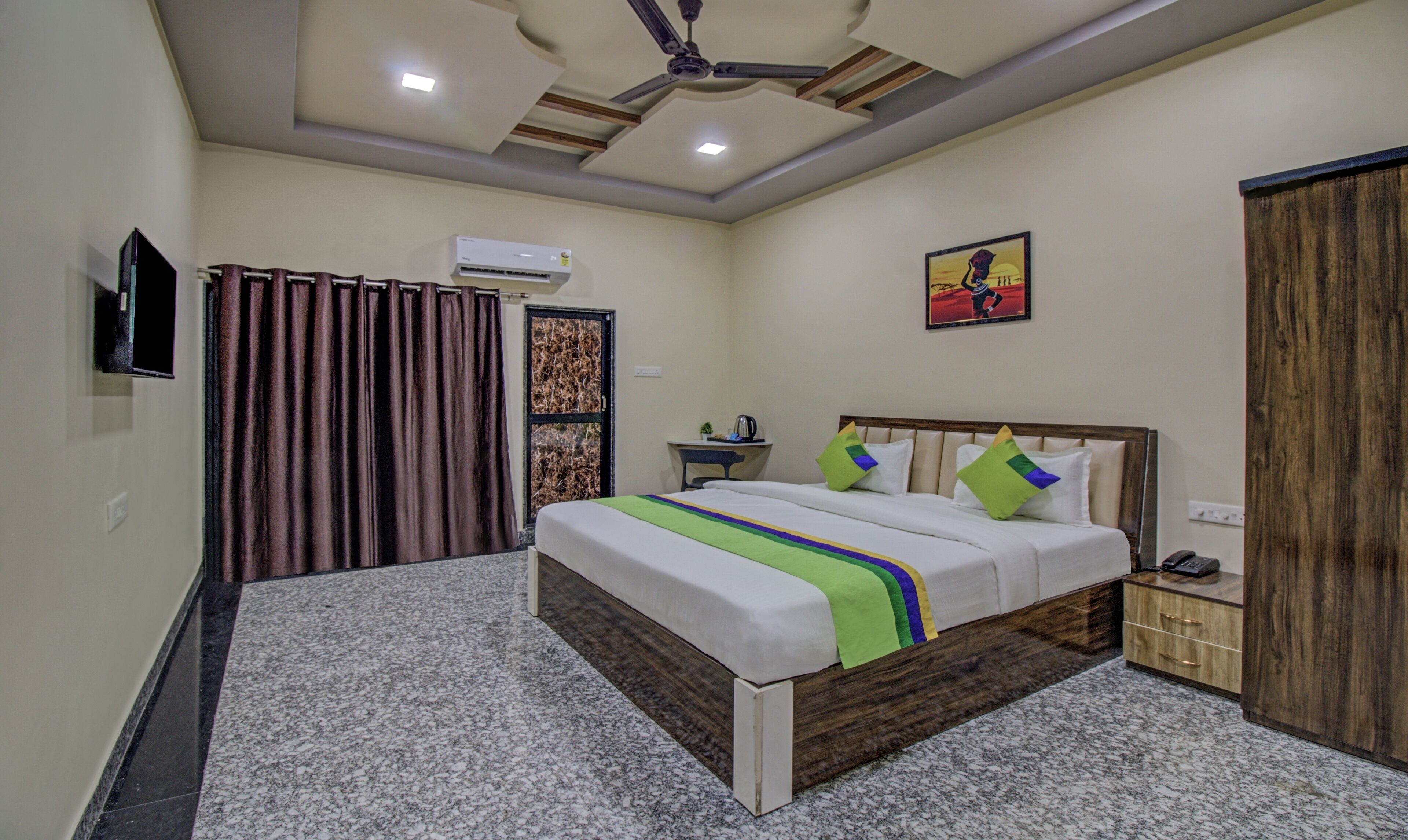 A bedroom with a bed, a desk, a chair, a wardrobe, a ceiling fan, and an air conditioning unit.