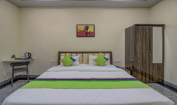 A hotel room with a bed, a desk with a coffee maker, a small plant, and a painting on the wall. - Treebo Royal, Chandrapur (Chandrapur)