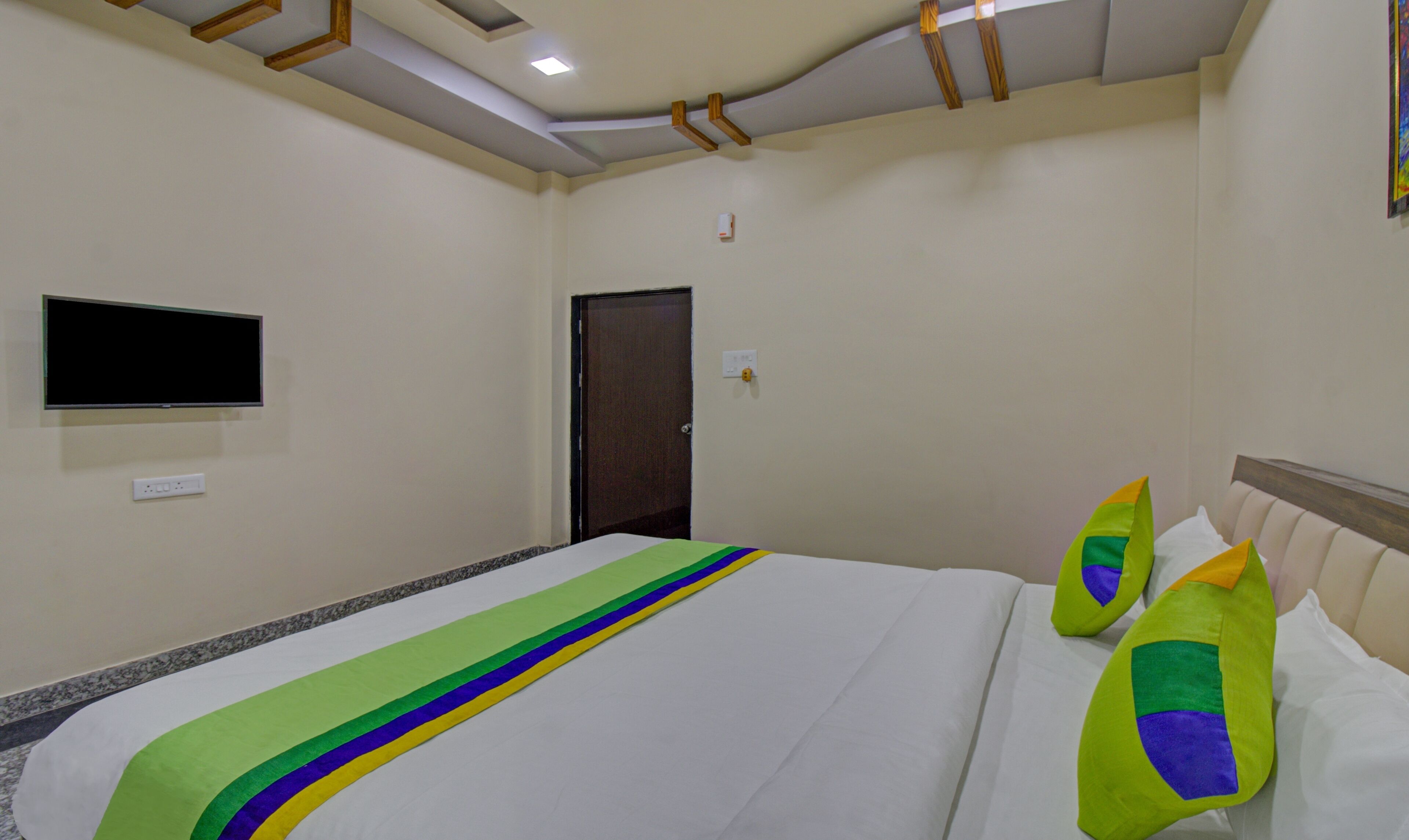 Una habitación de hotel con una cama, un televisor de pantalla plana montado en la pared y una puerta.