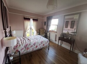 Classic bedroom with a large bed, bedside table, and dresser, offering a view of the outdoors.