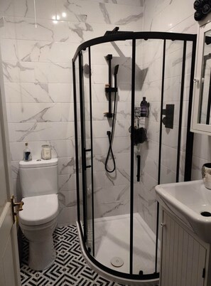 Bathroom features a curved shower enclosure with a glass door, handheld showerhead, and toilet.