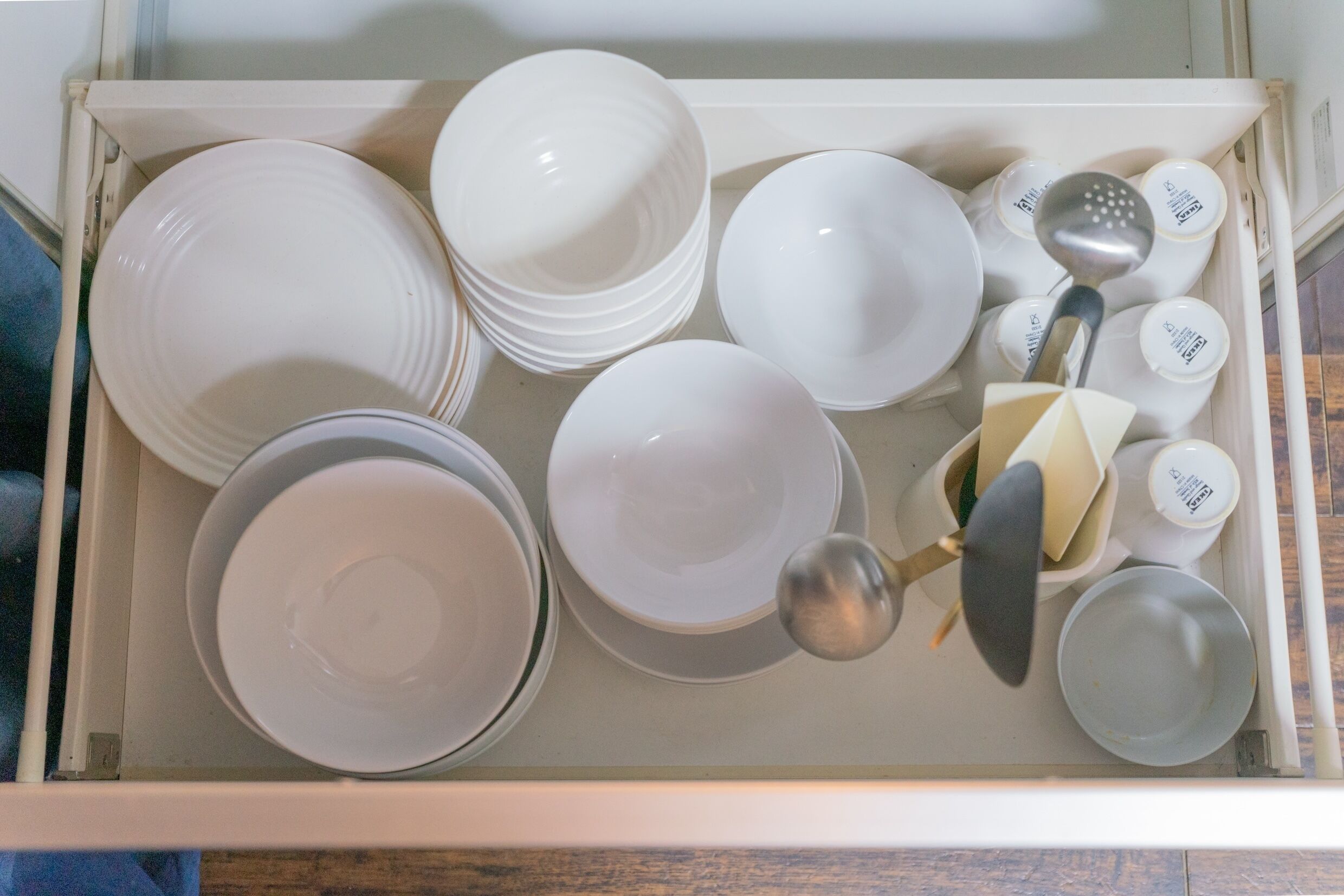 A drawer containing various white dishes, including plates, bowls, and a ladle.