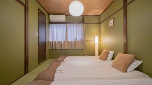 Ein Hotelzimmer mit zwei Betten, einer Holzbalkendecke, einem mit Vorhängen versehenen Fenster und einer wandmontierten Klimaanlage.