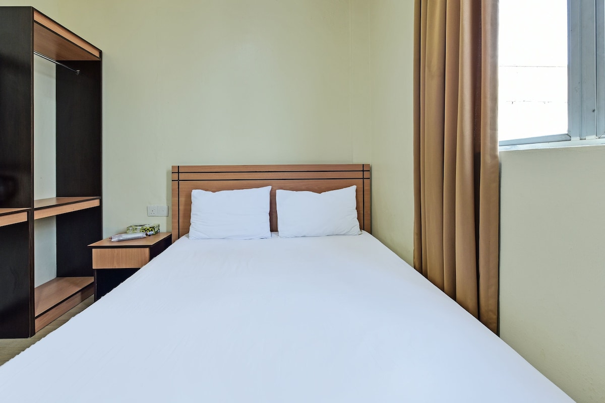 Una habitación de hotel con una cama grande, una mesita de noche de madera, un espejo y un ventanal con cortinas.