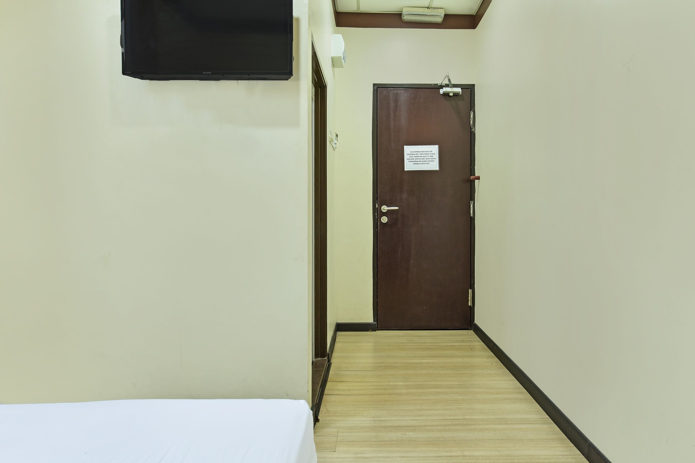 Un pasillo estrecho con suelo de madera, una cama a la izquierda y una puerta cerrada al final.