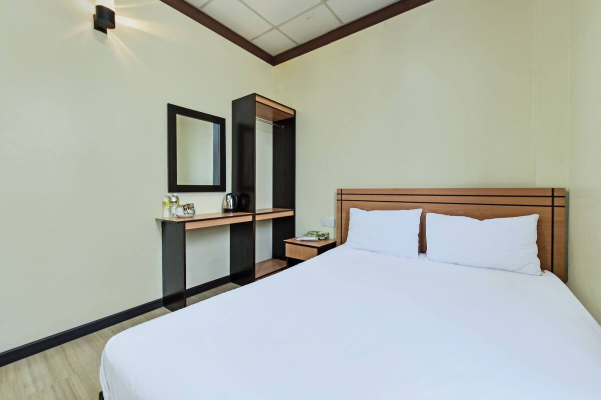 Een hotelkamer met een groot bed, een nachtkastje, een spiegel en een kleine tafel met een lamp.