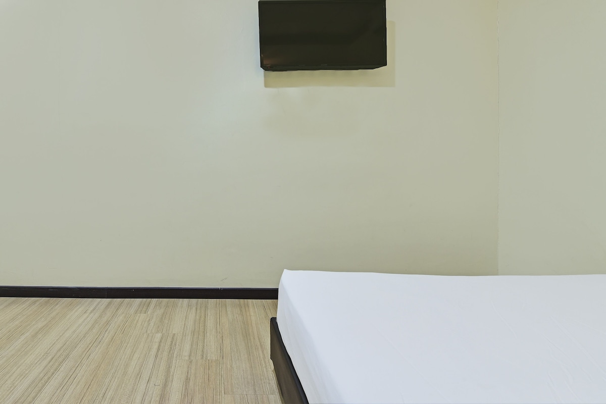 A room with a bed, a small window, and a wooden floor.