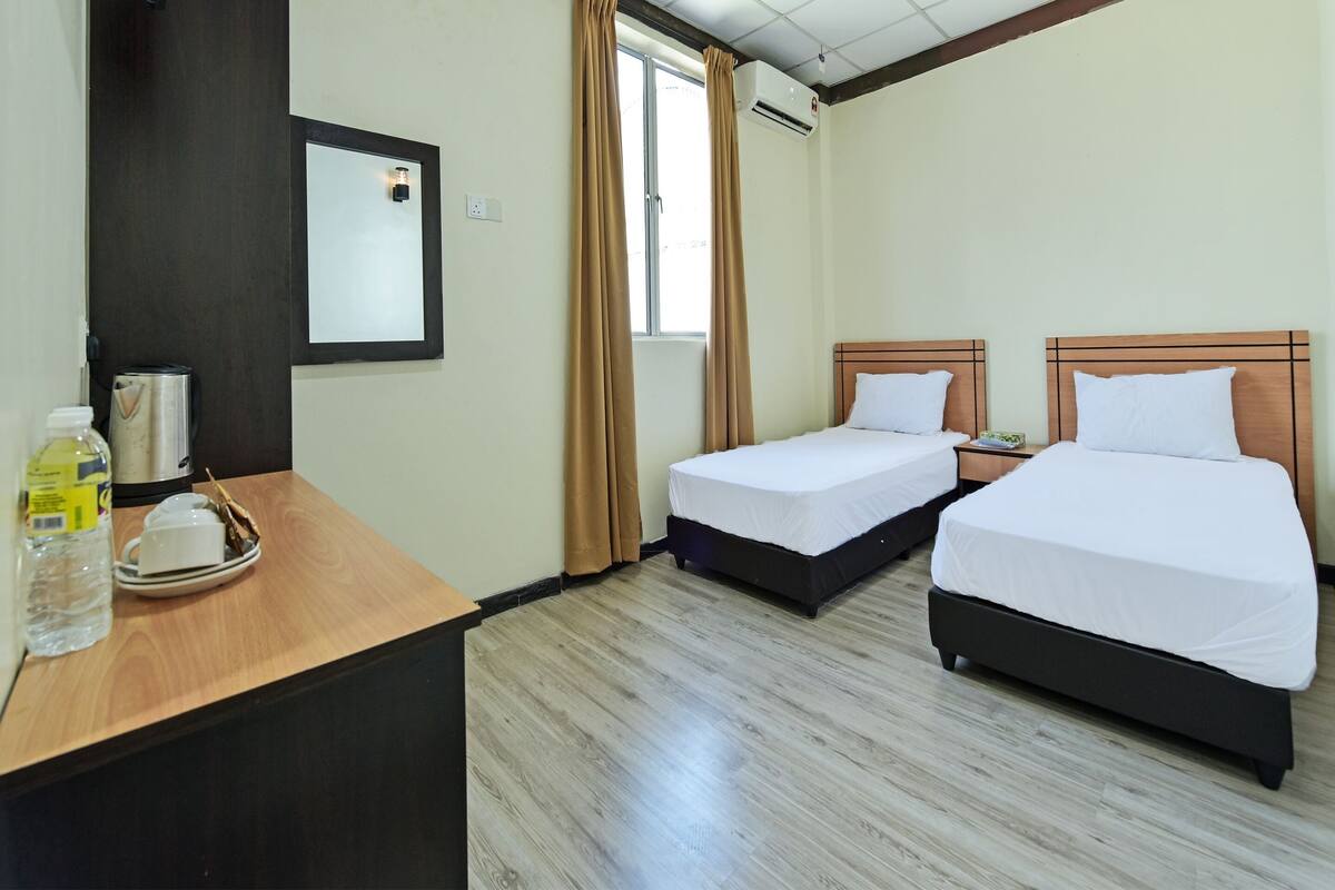 Een hotelkamer met twee enkele bedden, een houten bureau met een tray toiletartikelen en een raam met gordijnen.