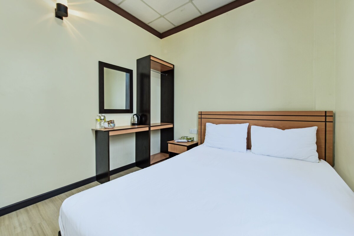 Een hotelkamer met een groot bed, een nachtkastje, een spiegel en een kleine tafel met een lamp.