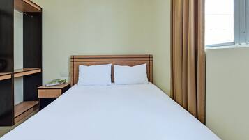 A hotel room with a large bed, a wooden nightstand, a mirror, and a window with curtains.