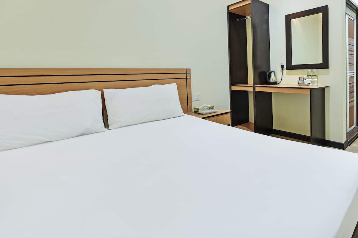 Een hotelkamer met een groot bed, een nachtkastje, een spiegel en een klein tafeltje met een waterkoker en flessen.