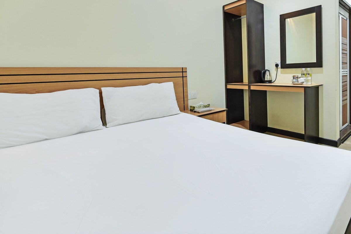 Een hotelkamer met een groot bed, een nachtkastje, een spiegel en een klein tafeltje met een waterkoker en flessen.