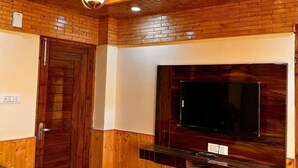 A room with wooden paneling, a large TV mounted on the wall, a round table, and a door with a handle. - Wood Crista Retreat by Park Tree (Theog)