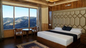 A bedroom with a large bed, a wooden headboard, a dining table with chairs, and a view of mountains through large windows. - Wood Crista Retreat by Park Tree (Theog)