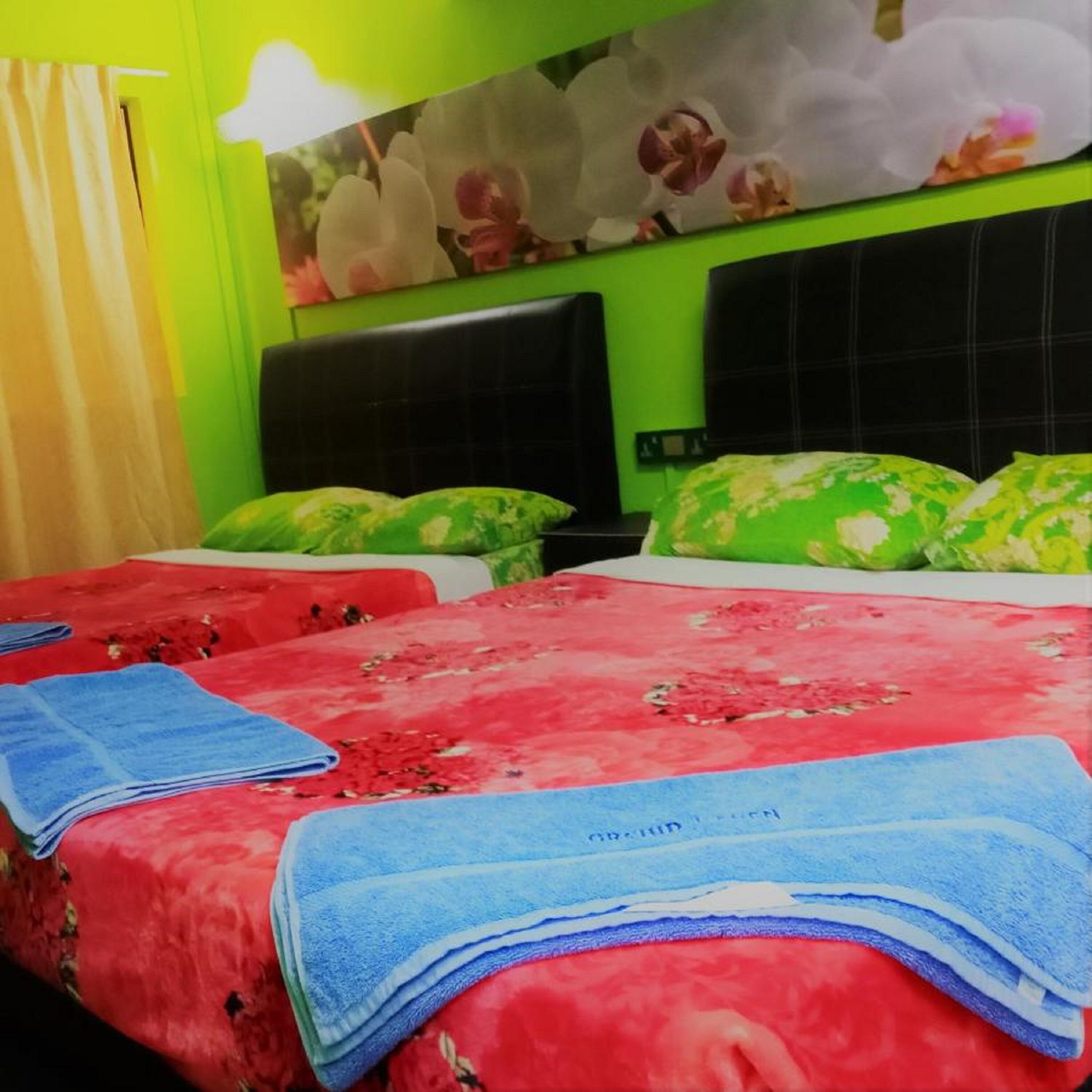 A hotel room with two beds, each with a red floral bedspread and green pillows. There are blue towels on the beds.