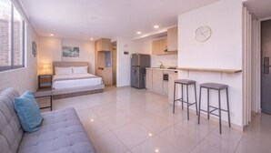 Un apartamento moderno con un dormitorio, kitchenette y sala de estar con sofá y taburetes de bar.