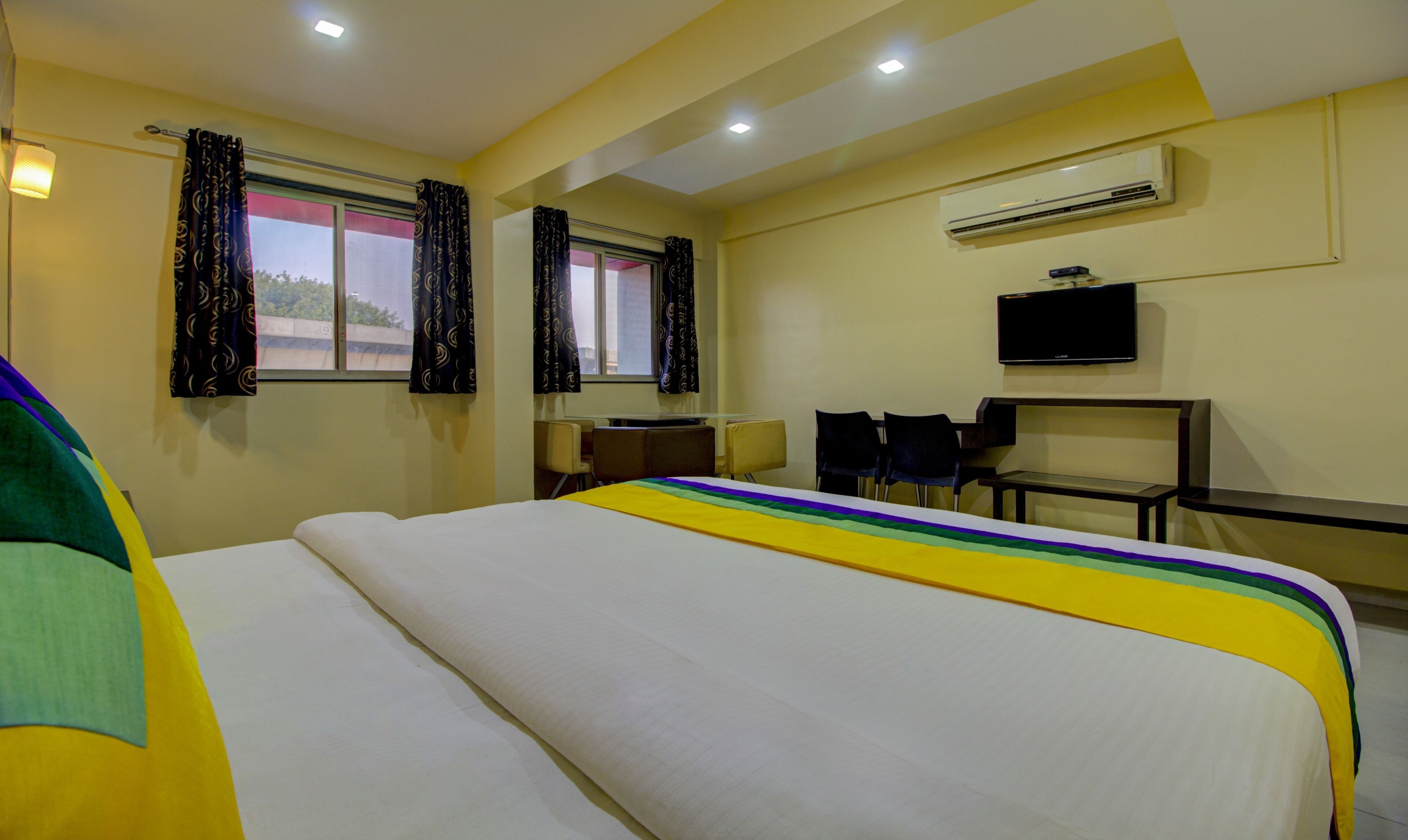 A hotel room with a bed, a desk, a chair, an air conditioner, and a television.