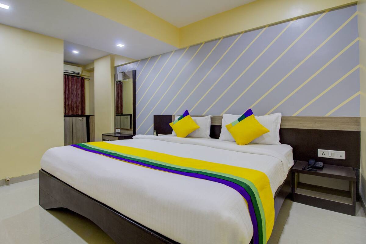 Una habitación de hotel con una cama grande, una mesita de noche, un espejo y un armario.