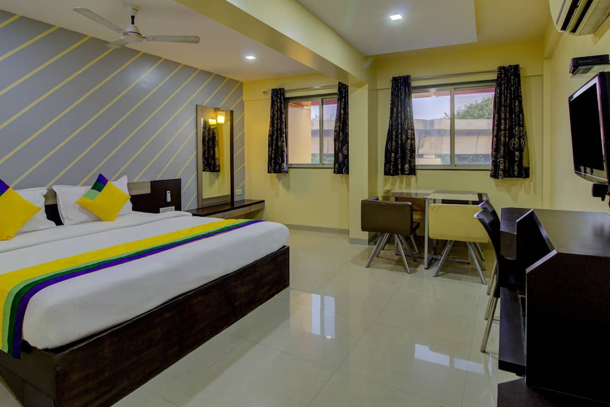 Habitación de hotel con cama, escritorio, silla, televisor y ventilador de techo.