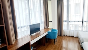 Ein Hotelzimmer mit einem Holztisch, einem blauen Sessel, einem Bett und großen Fenstern mit Vorhängen.