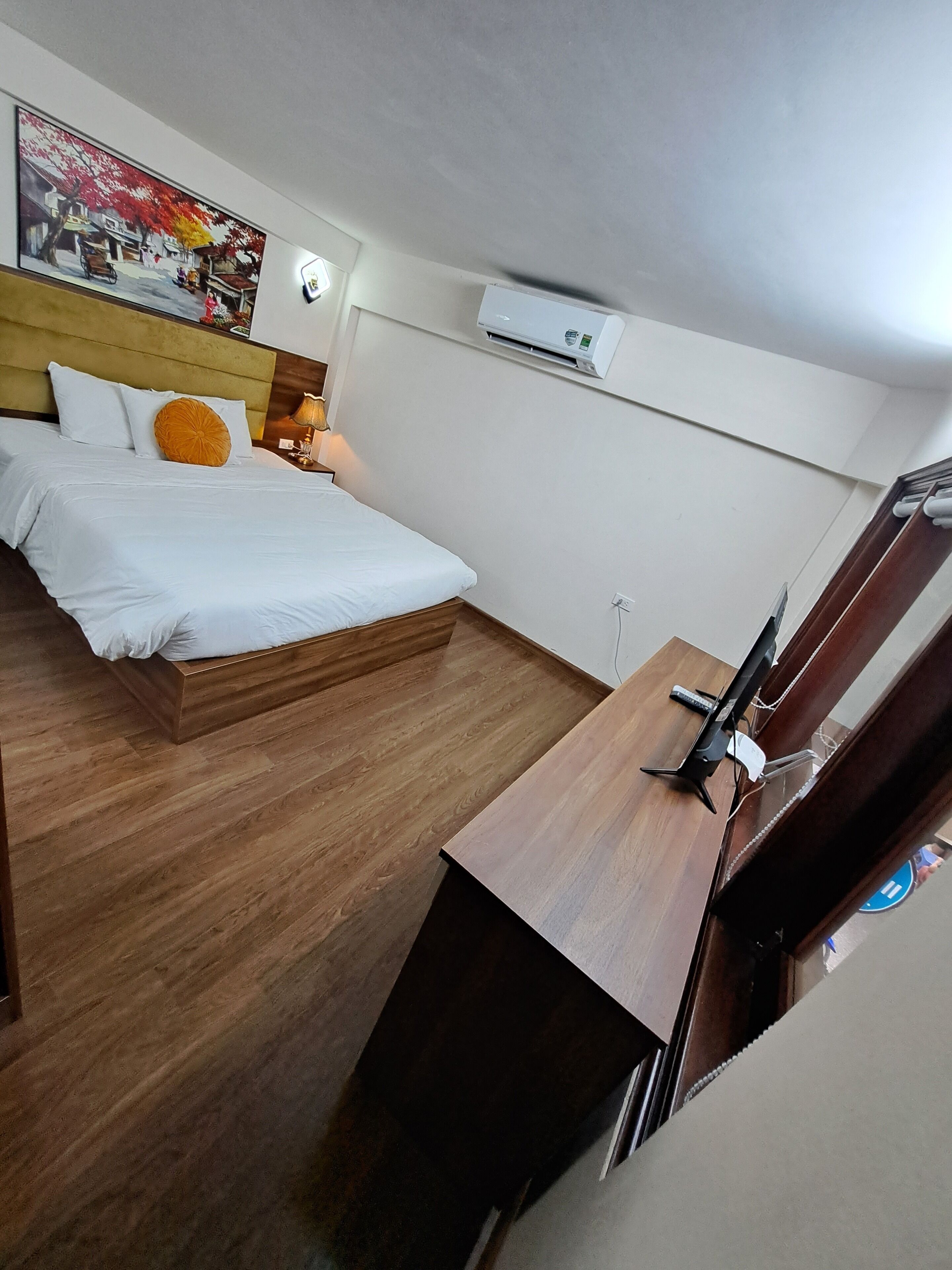 A hotel room with a bed, wooden flooring, a TV, and an air conditioning unit.