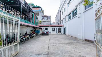 Una calle estrecha con motocicletas y un automóvil estacionados, edificios con balcones y un cielo despejado.
